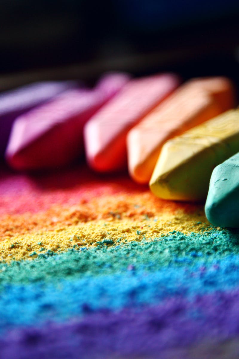 Close-up of vibrant colored chalks forming a rainbow pattern against a dark background.
